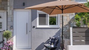 Un bâtiment moderne à la façade grise, avec une porte blanche et un petit patio agrémenté d’une chaise et d’un parasol.