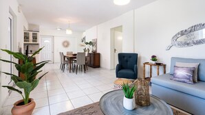 Uma sala de estar moderna com sofá, área de jantar com cadeiras, uma poltrona azul e uma planta em vaso.