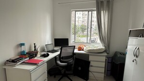 Ein kleiner Büroraum mit Schreibtisch, Stuhl, Computer und einem Fenster mit Blick auf Gebäude.