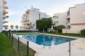 Une piscine entourée d’immeubles d’habitation, sous un ciel dégagé, avec un poste de surveillance pour les sauveteurs.