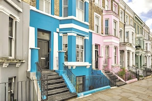 A row of colorful terraced houses with distinct architectural styles, including a blue house with a black door and white trim, a pink house with a white door, and a green house with a white door. - The Notting Hill Blue Palace (Greater London)