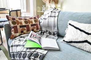Ein Sofa mit einem gemusterten Überwurf, ein Kissen mit geometrischem Muster und ein Buch.