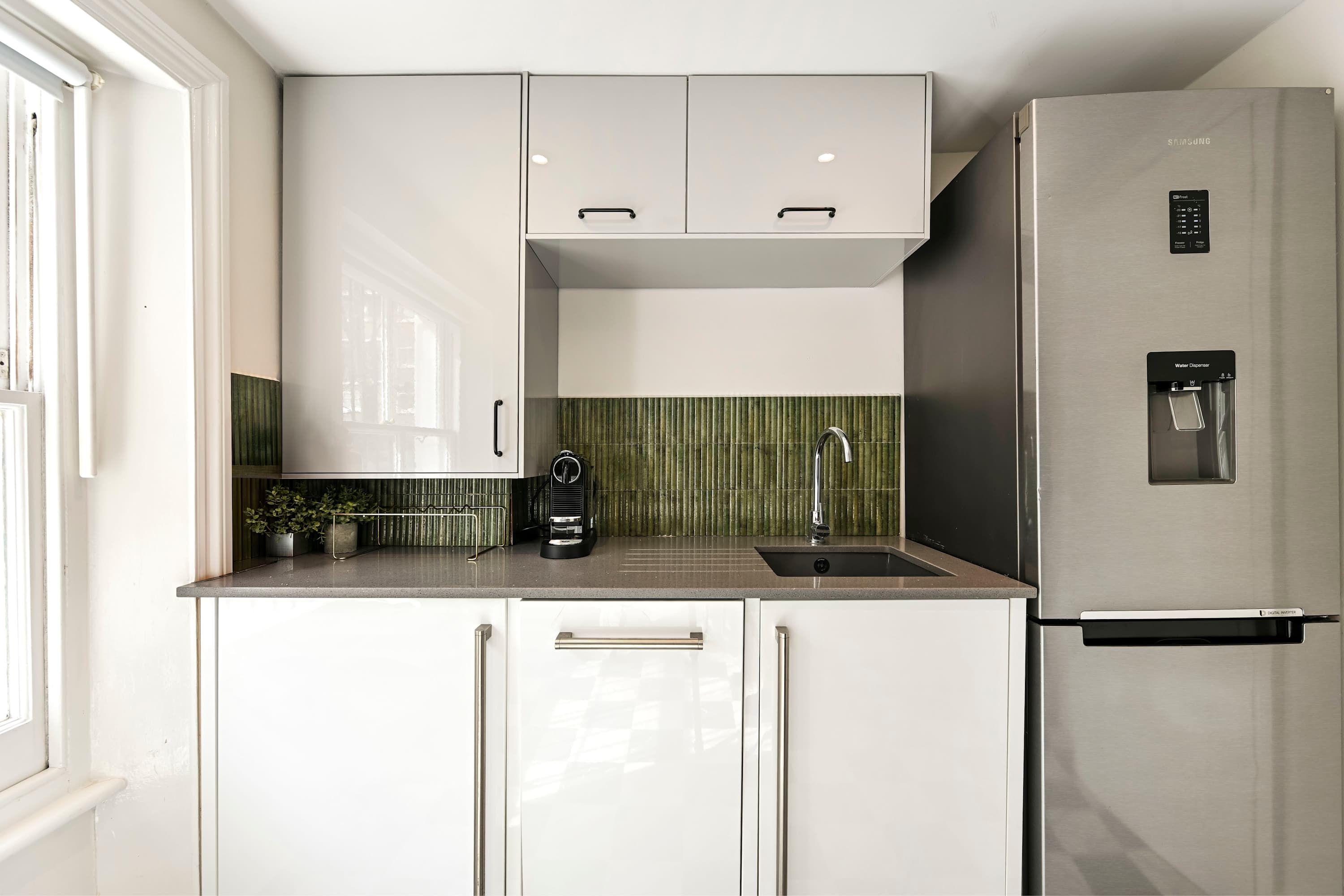 Une cuisine moderne avec des meubles blancs, un réfrigérateur en acier inoxydable, un distributeur d’eau et une machine à café.
