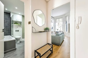 A modern bathroom with a bathtub, toilet, and shower. There is a bench in the hallway and a mirror on the wall. - The Notting Hill Blue Palace (Greater London)