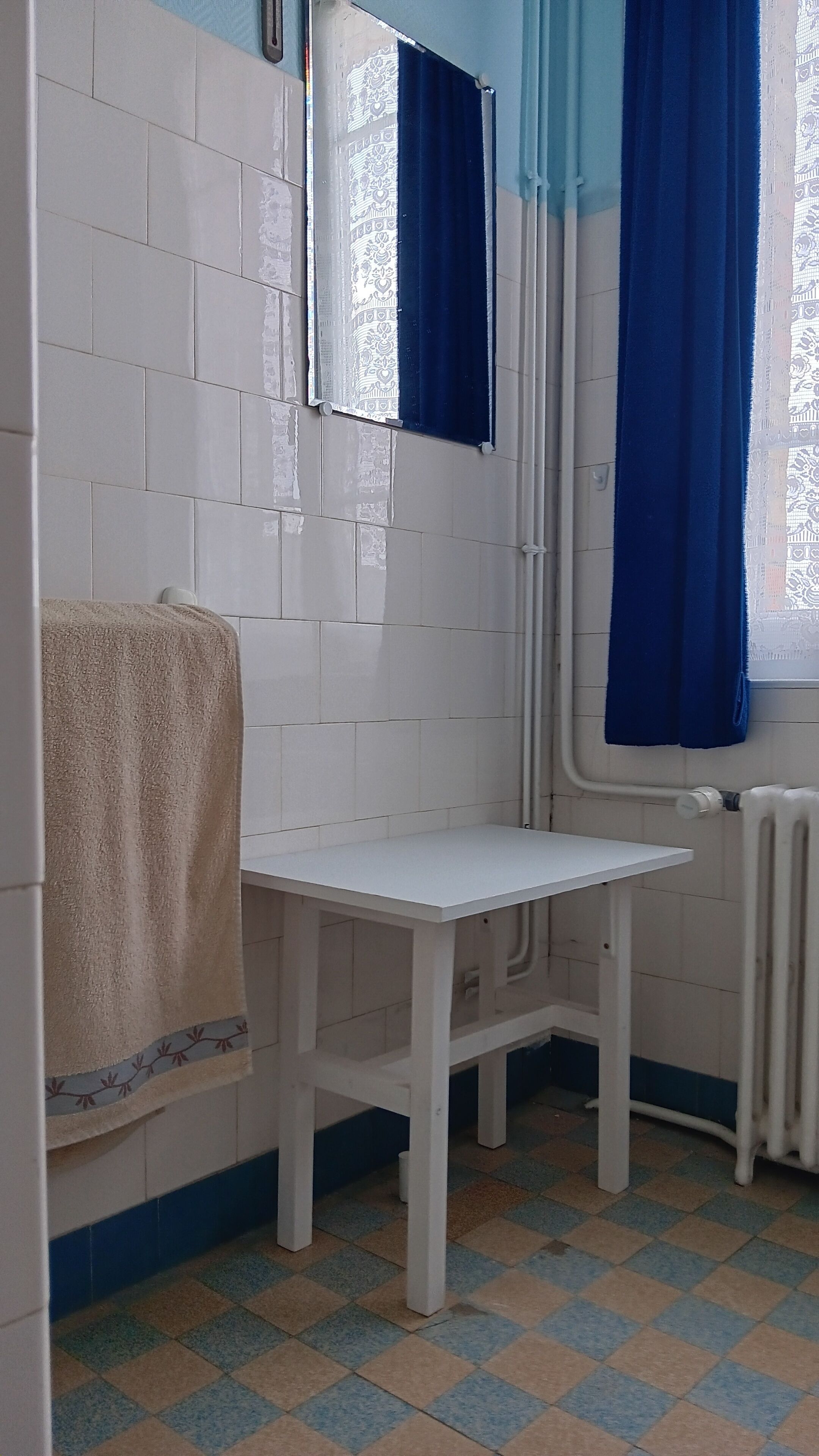 A bathroom with white tiled walls, a white sink, a towel, and a window with blue curtains.