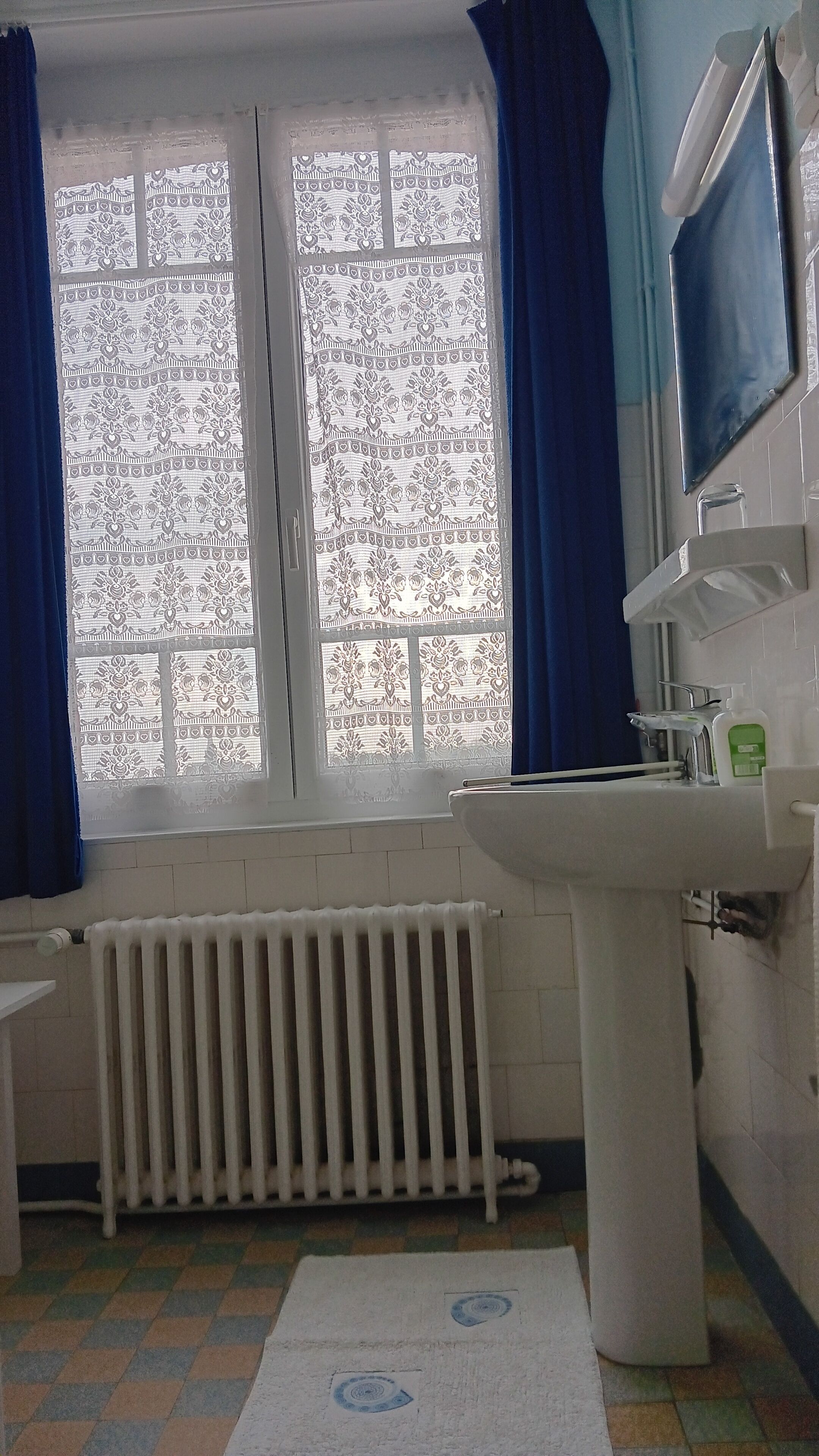 Une salle de bain avec une fenêtre, un radiateur, un lavabo et un miroir.