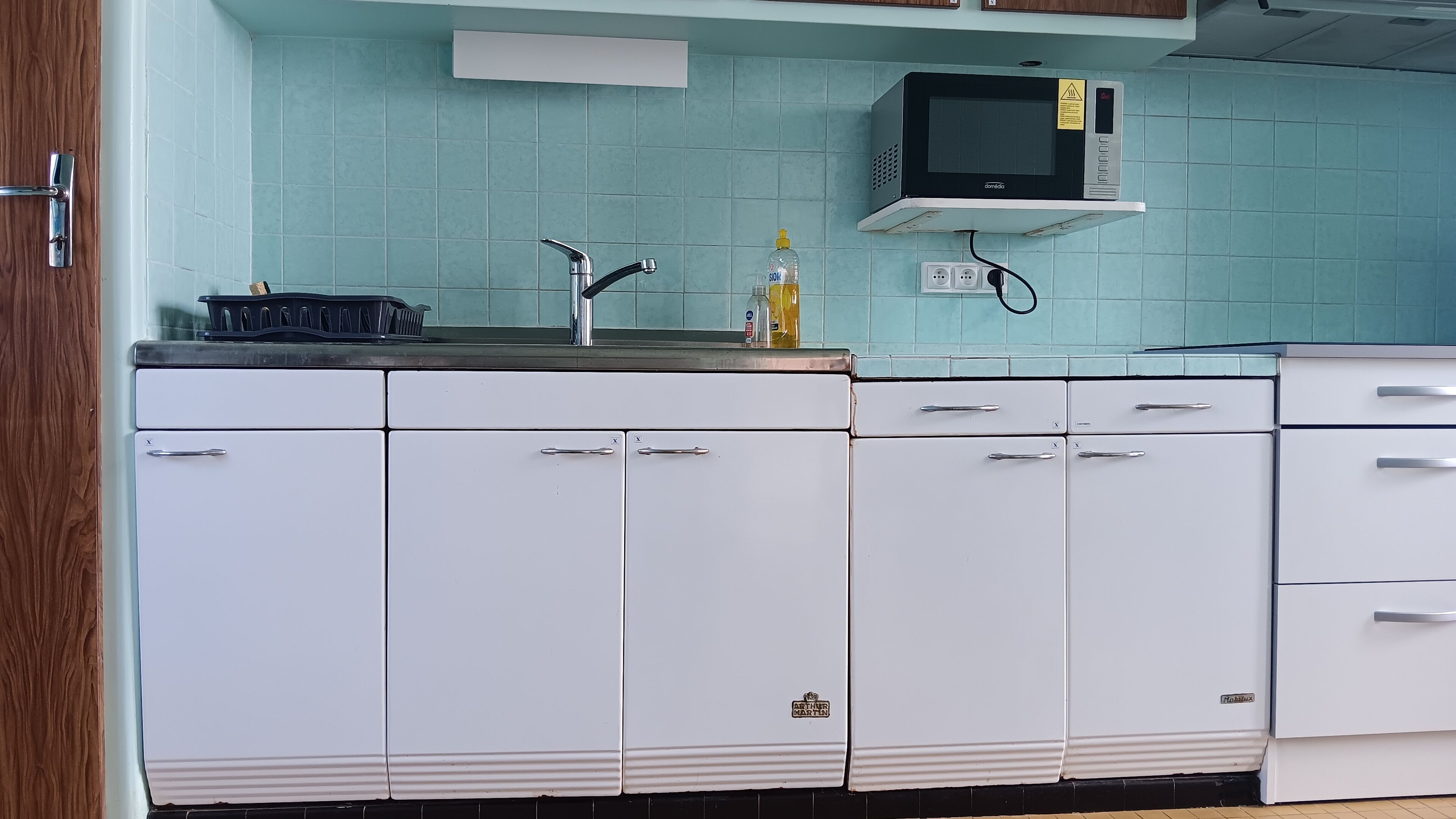 Una cocina con armarios blancos, un microondas, un lavabo y un grifo.
