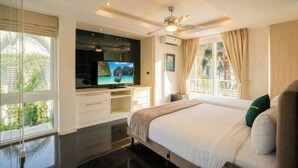 A bedroom with a bed, a TV, a ceiling fan, and a window with curtains. - Luxury 5BR Villa Jomtien - Pool, Sports & Karaoke Close to the beach of pattaya (เมืองพัทยา)