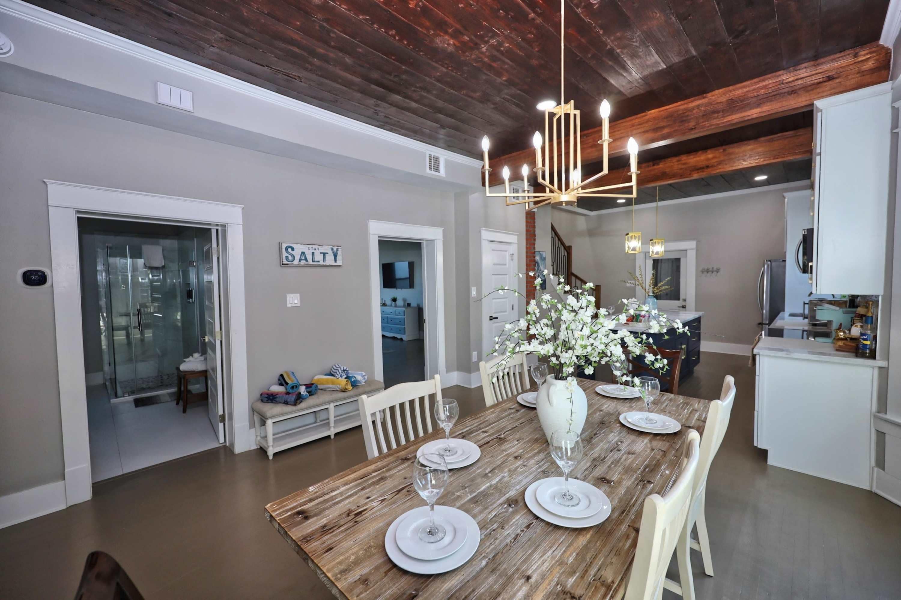 A dining area with a wooden table set for four, a chandelier, and a sign that reads 'STAY'.