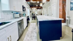 A modern kitchen with white cabinets, a central island, and pendant lighting. - Coastal Cove Near Beach (Galveston)