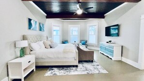 A bedroom with a bed, bedside tables, a dresser, a ceiling fan, and a TV mounted on the wall. - Coastal Cove Near Beach (Galveston)