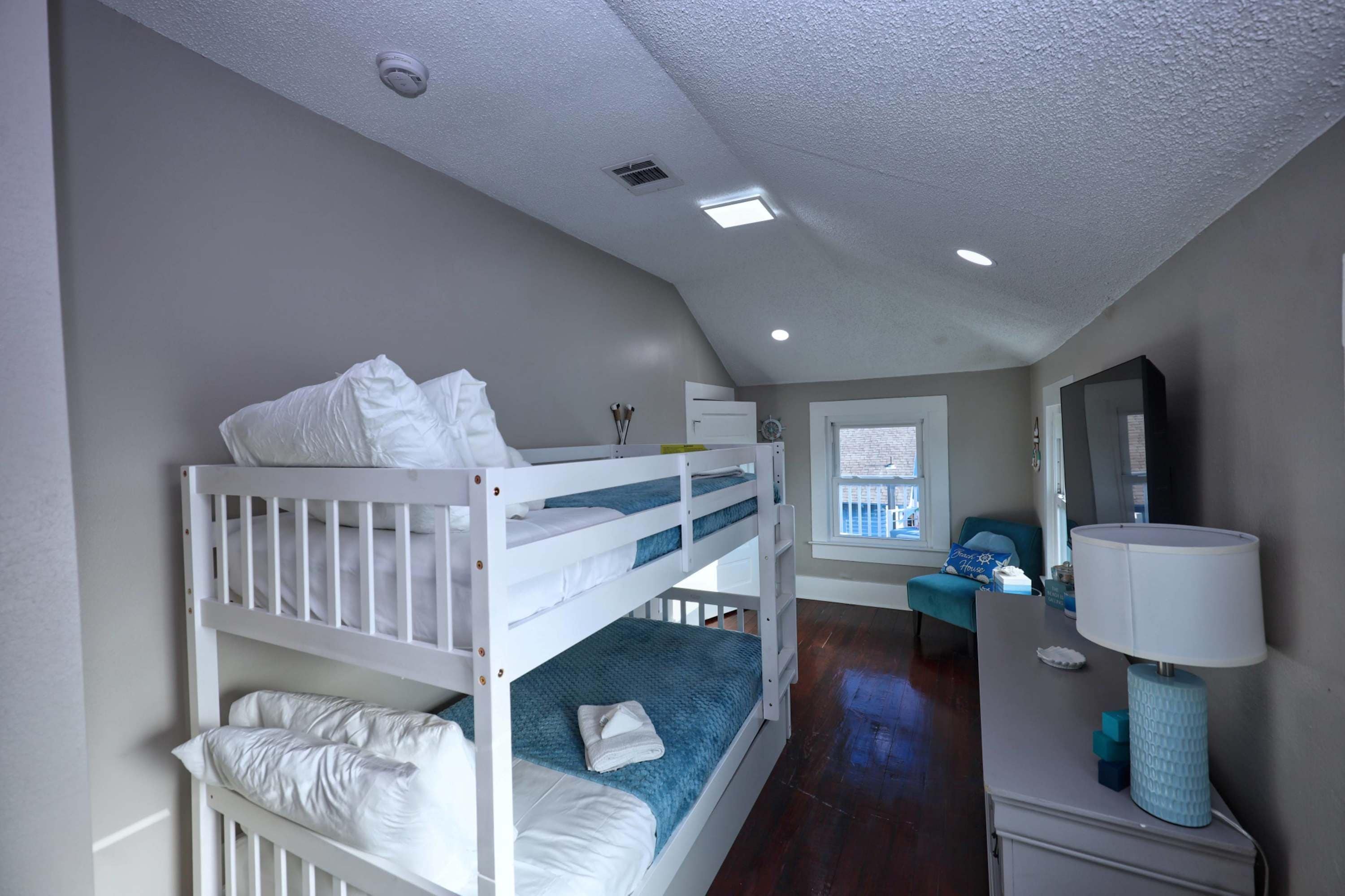 A room with bunk beds, a desk, a chair, a lamp, and a window with a view.