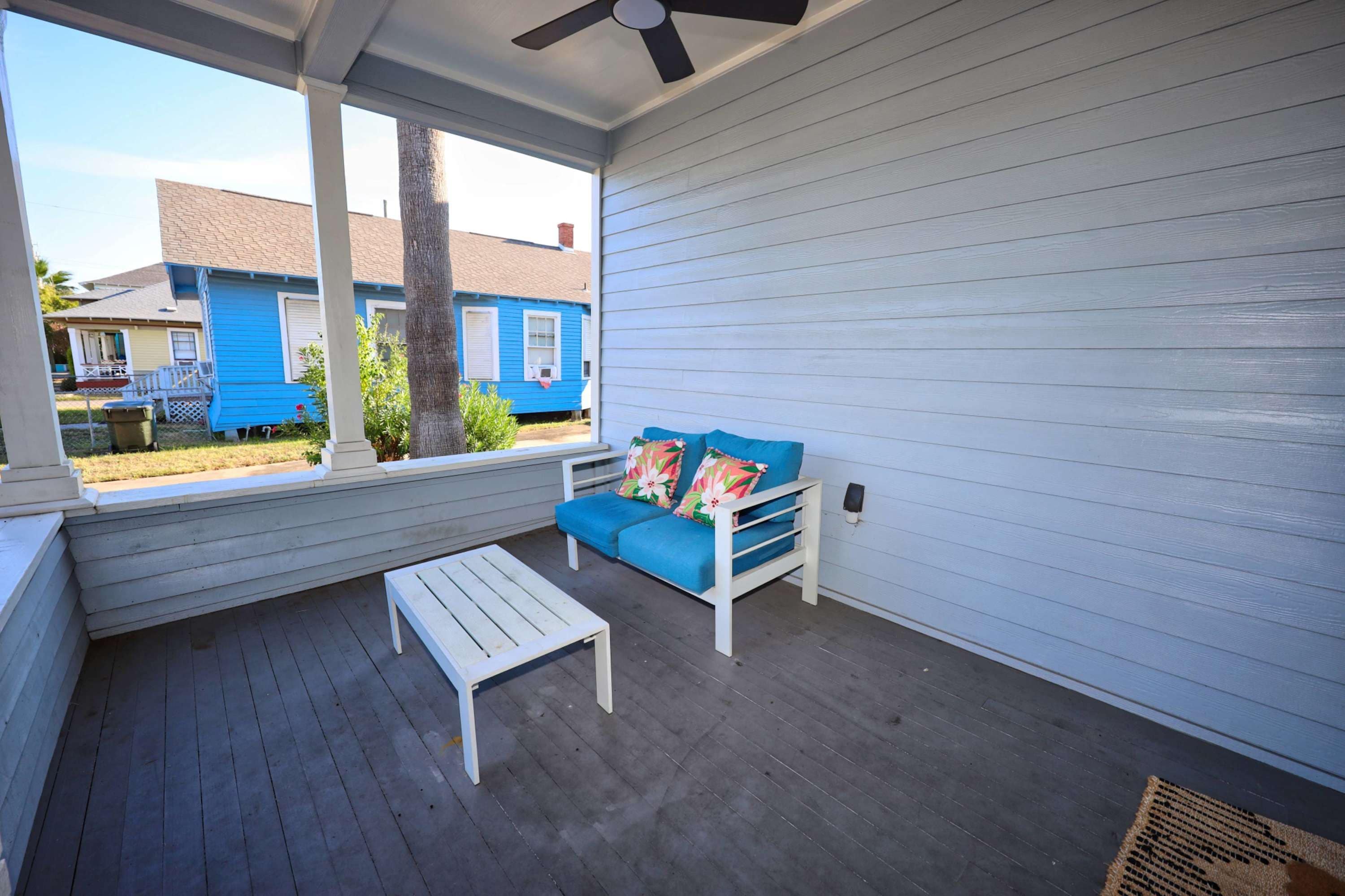 A covered porch with a white bench and a blue sofa with floral cushions.