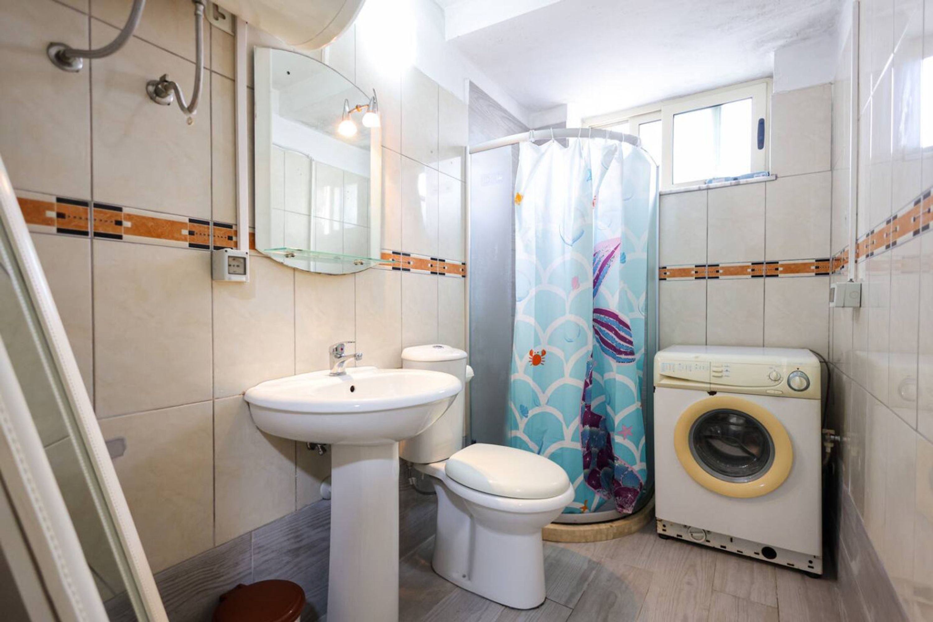 Une salle de bain équipée d’un lavabo, de toilettes, d’un rideau de douche et d’un lave-linge.