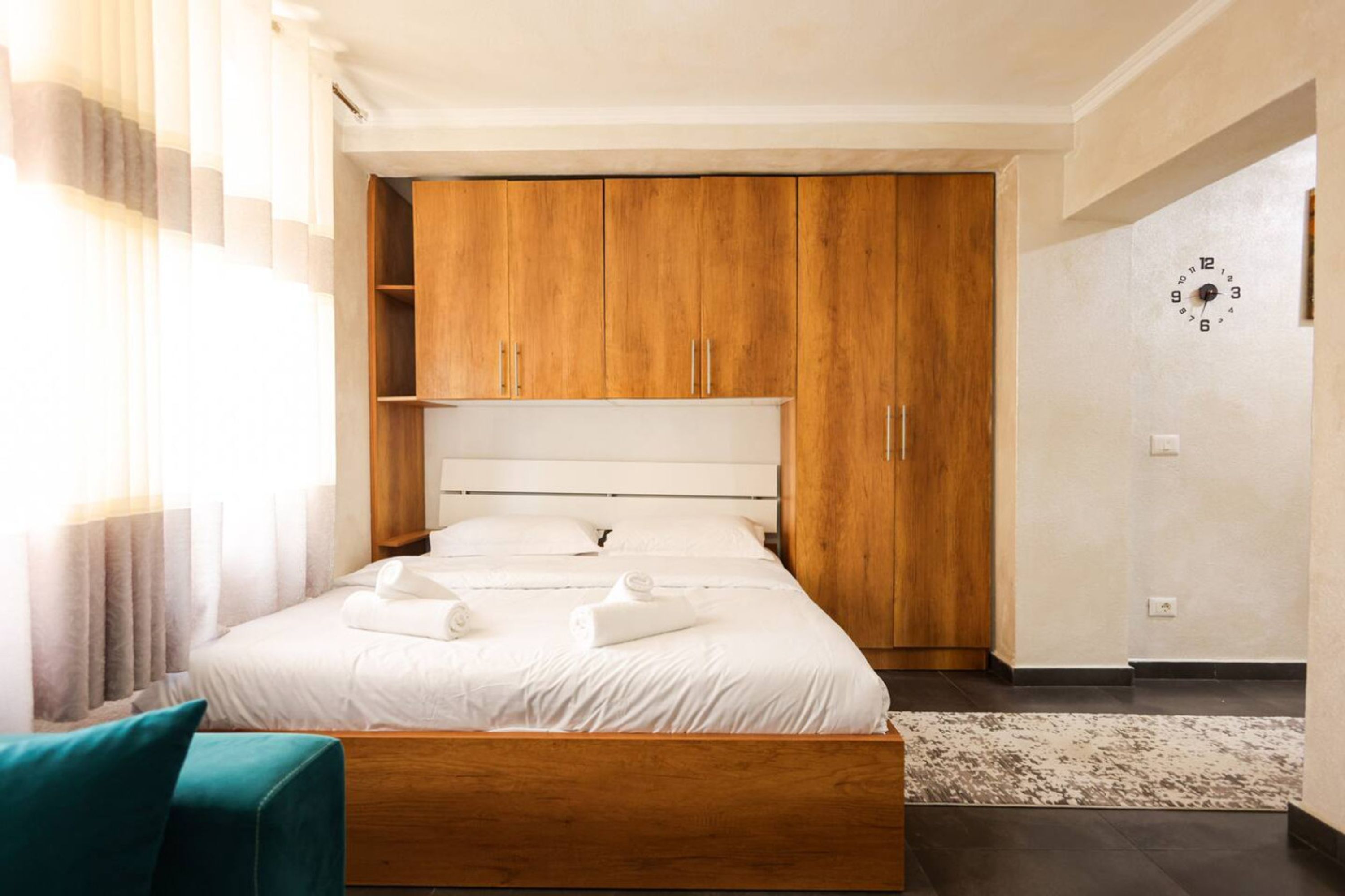 A hotel room with a bed, wooden wardrobe, and a clock on the wall.