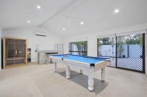 A pool table in a room with a ceiling fan, a window, and a door with a view of the outside.