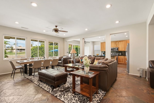 A spacious living room with a dining area, a kitchen, and a ceiling fan.