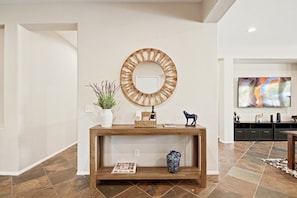 A living room with a wooden console table, a round mirror, a potted plant, a vase, and a television on a wall.