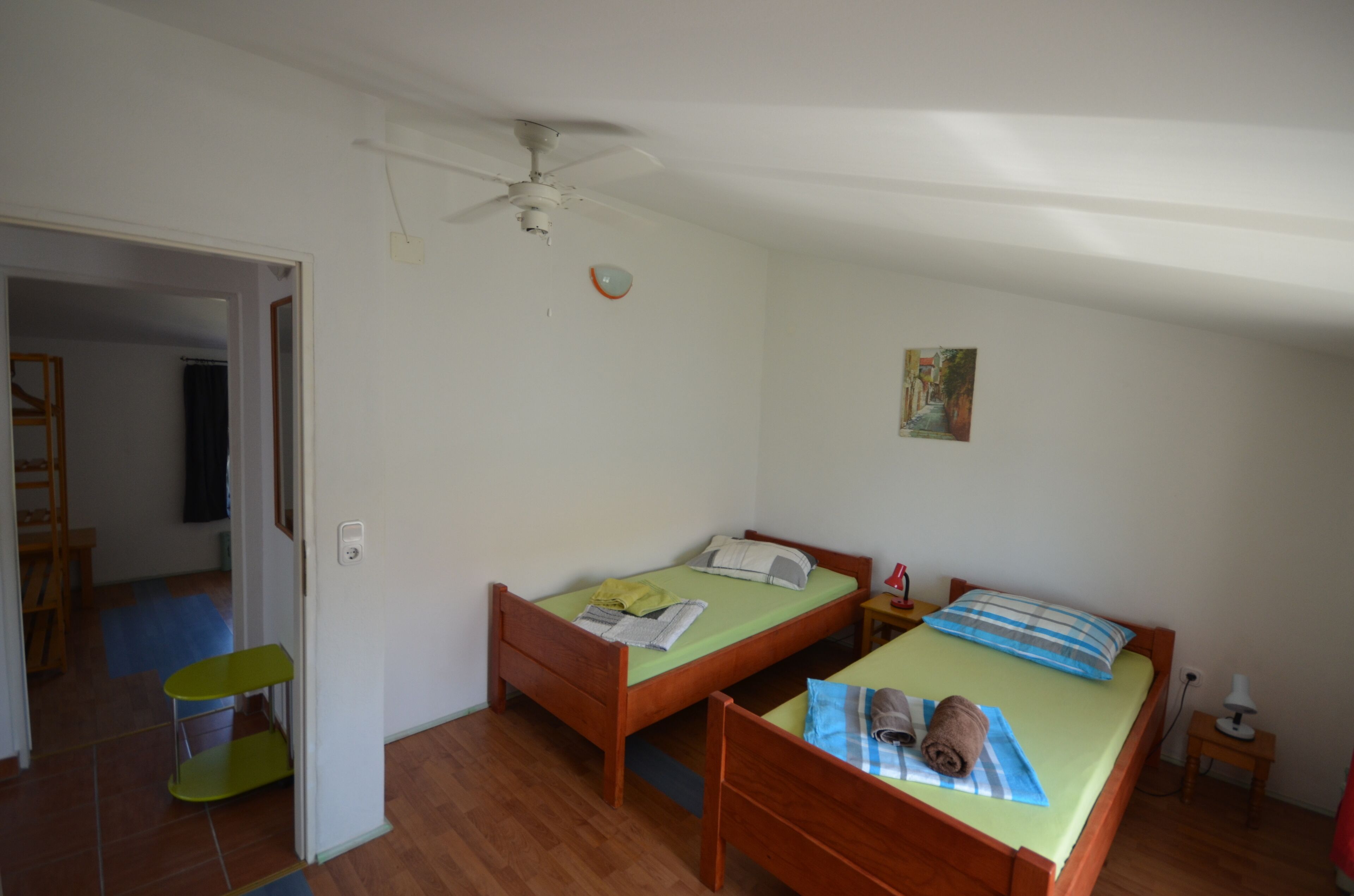 A bedroom with two wooden beds, a ceiling fan, a small bedside table, and a door leading to another room.