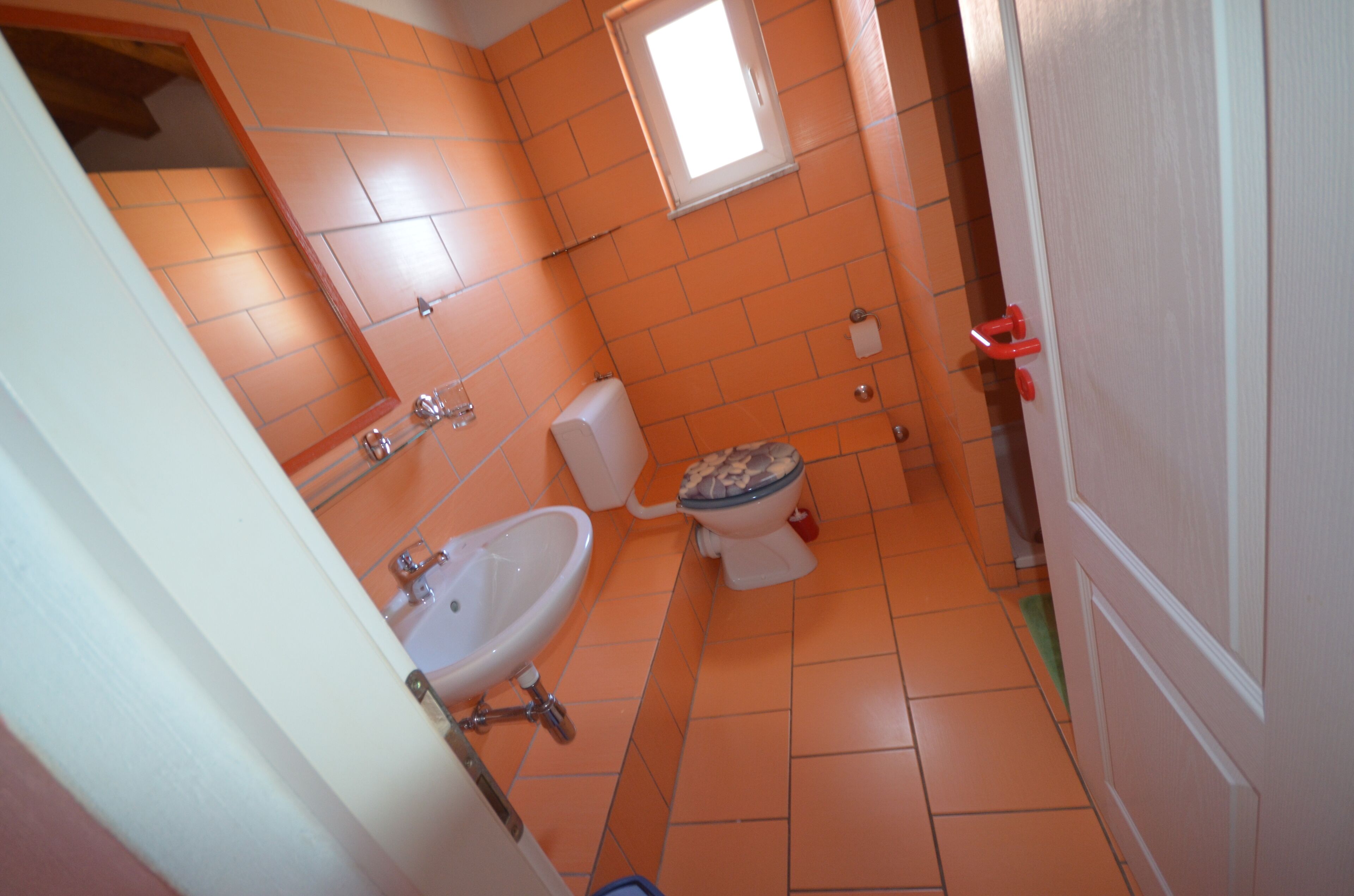 Un baño con azulejos naranjas, un lavamanos blanco y un inodoro.