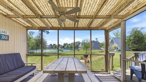 A covered patio with a wooden table and benches, a ceiling fan, and a view of a lake and grassy area. - Juniper Presents: Chalet #71 Near Pickleball Courts & Walk to Beach (Stevensville)