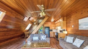 A wooden cabin interior with a staircase, a living room with a sofa and coffee table, and a kitchen area. - Juniper Presents: Chalet #71 Near Pickleball Courts & Walk to Beach (Stevensville)