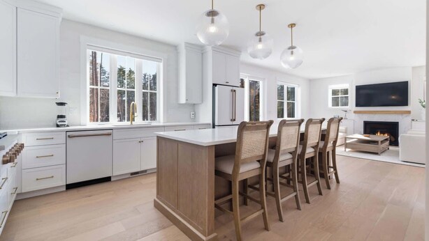 A modern kitchen with white cabinetry, a central island, and a dining area with chairs. - Van Duyne North Airy Escape (Ogunquit)
