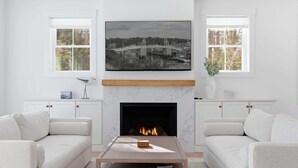 A living room with a fireplace, white sofas, a coffee table, and a large framed picture above the fireplace. - Van Duyne North Airy Escape (Ogunquit)