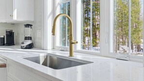 A modern kitchen with a stainless steel sink, a gold faucet, and a coffee maker. - Van Duyne North Airy Escape (Ogunquit)