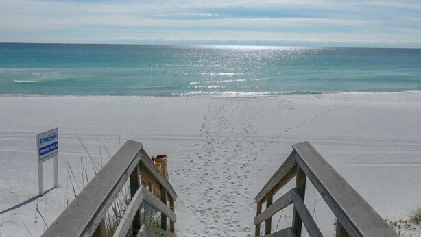 A beach with a wooden walkway leading to the water, a sign indicating it's a private beach, and footprints in the sand. - Heavenly Par-adise 2‑Bedroom Villa Overlooking the Golf Course Seascape (Miramar Beach)