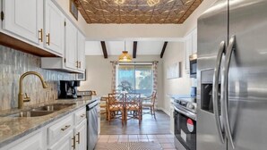 A modern kitchen with white cabinets, a stainless steel refrigerator, and a dining area with a table and chairs. - Heavenly Par-adise 2‑Bedroom Villa Overlooking the Golf Course Seascape (Miramar Beach)