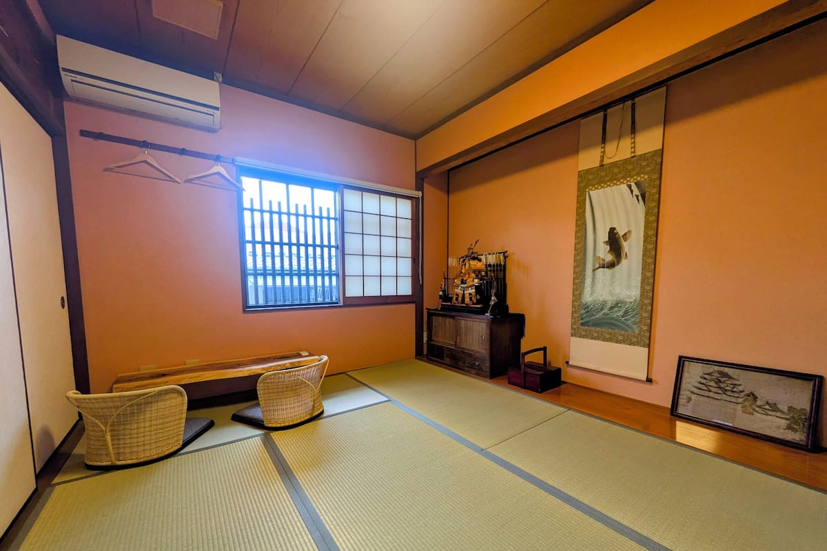 Une pièce avec un sol recouvert de tatamis, une cloison coulissante de style shoji, un panier suspendu et une peinture traditionnelle japonaise.