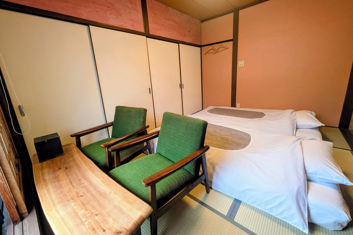 Une pièce comprenant un lit, deux fauteuils verts, une table en bois et une armoire.