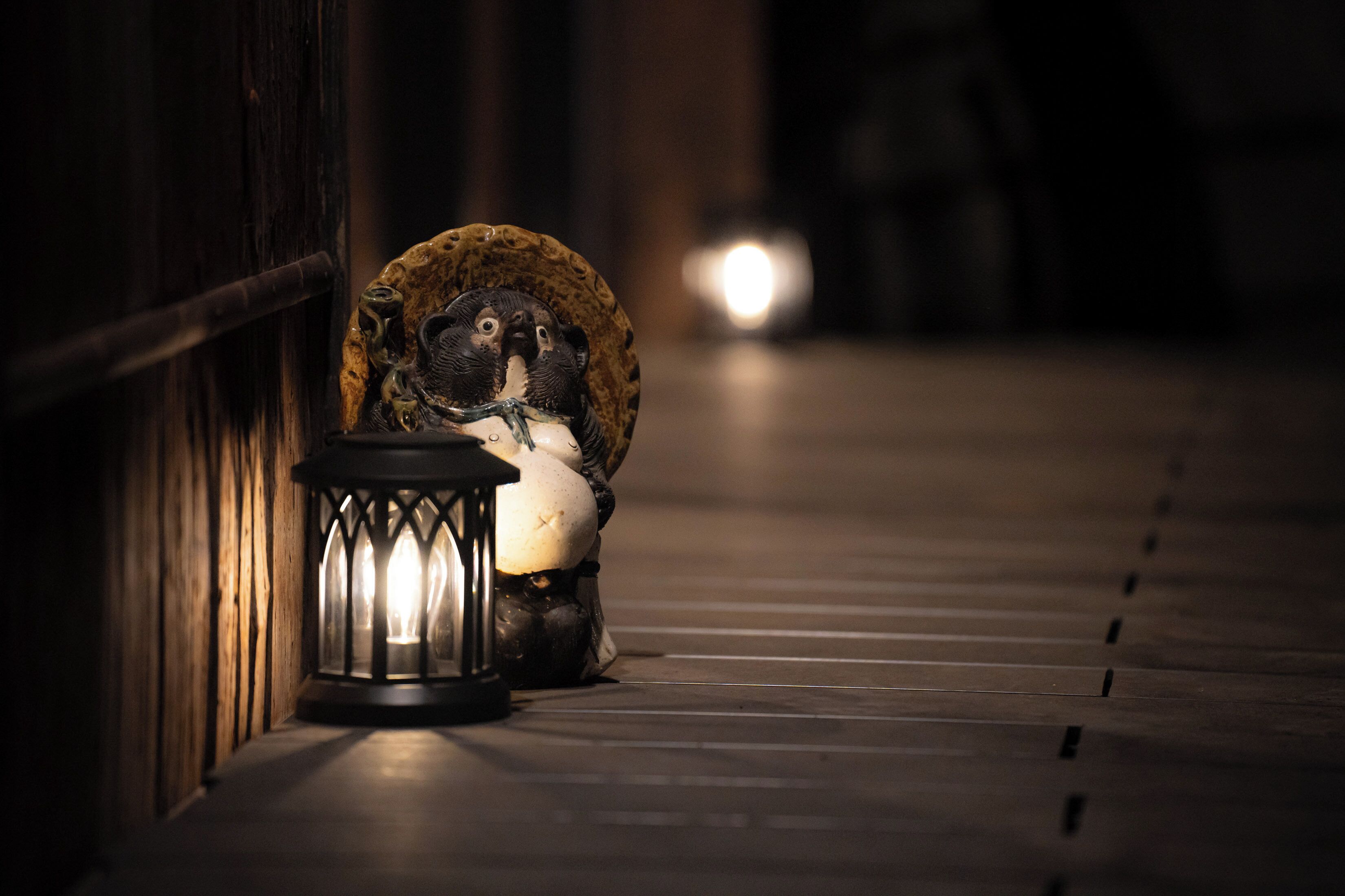 A narrow corridor with a wooden railing, a decorative lantern, and a statue.