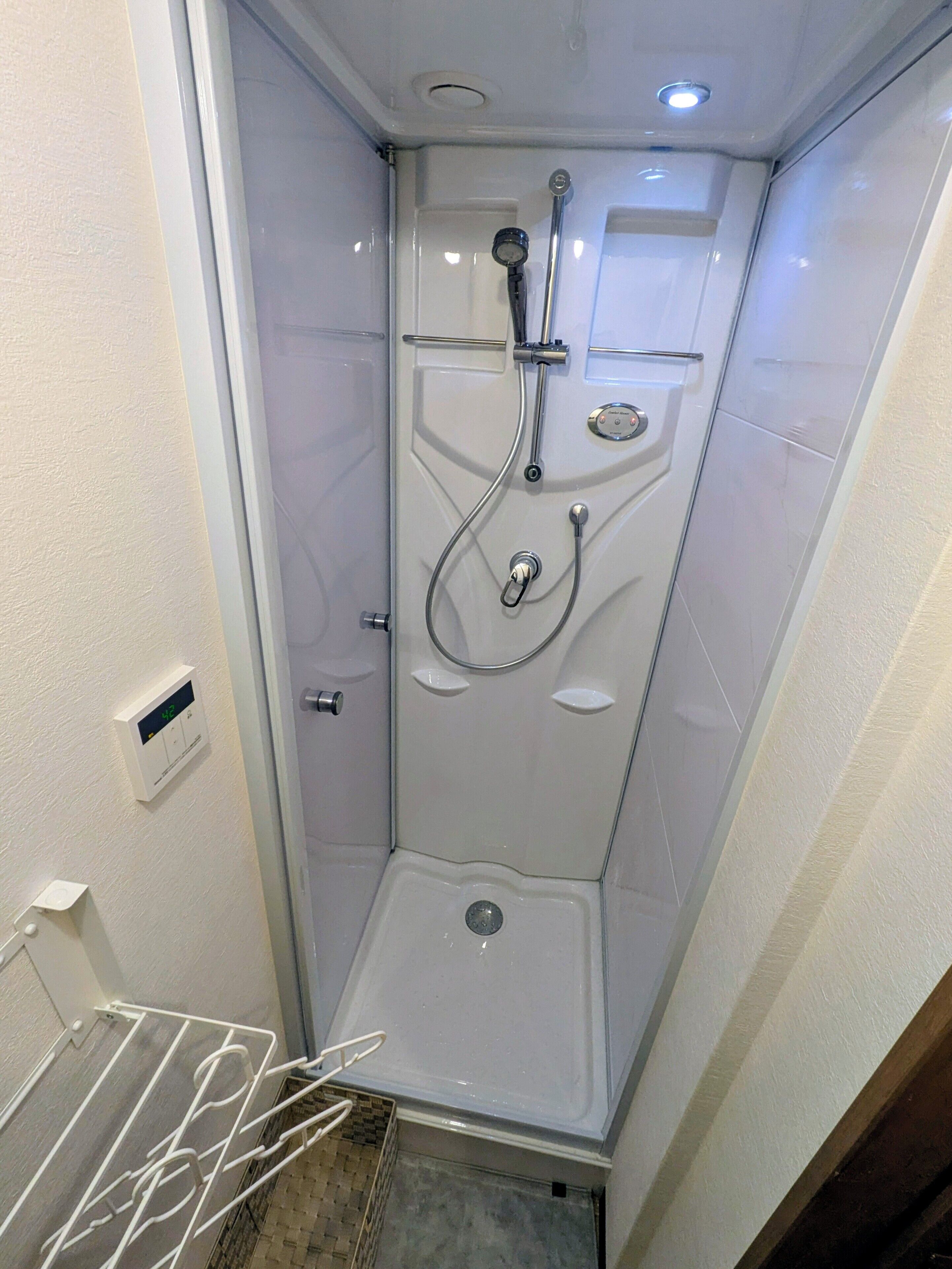 A small, enclosed shower stall with a control panel, a handheld showerhead, and a wall-mounted faucet.