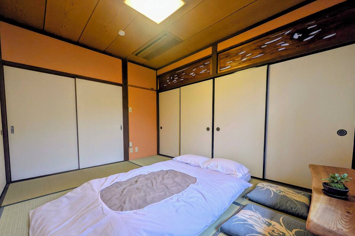 Une pièce de style japonais traditionnel, avec un sol recouvert de tatamis, un futon servant de lit, des portes coulissantes et une petite table agrémentée d’une plante.
