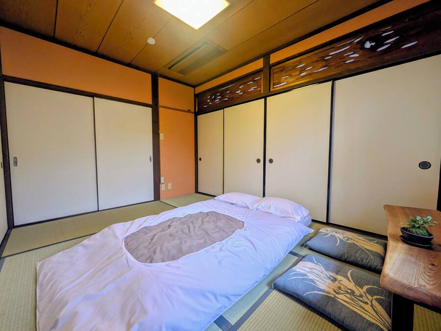 Una habitación tradicional japonesa con suelo de tatami, futón, puertas correderas y una pequeña mesa con una planta.