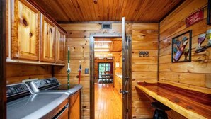A wooden cabin interior with a kitchen area, a bar, and a dining space. - New! Play in Lukfata Creek! Hot Tub! Fire pit! (Broken Bow)