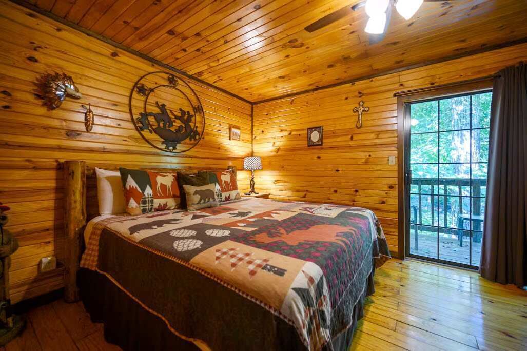 A wooden cabin bedroom with a bed, a window, and a door.