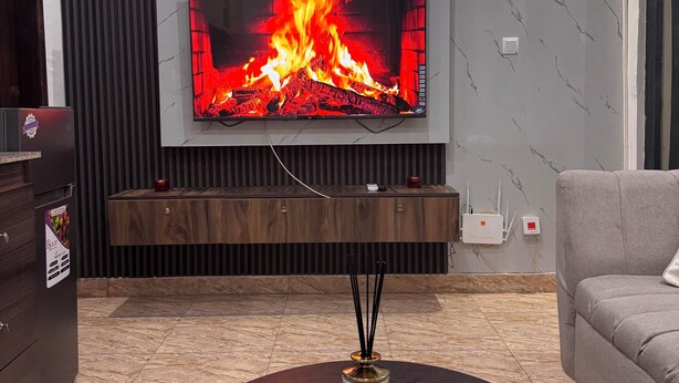 Una sala moderna con televisor de pantalla plana, chimenea, aparador de madera oscura y sofá gris.