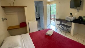 Een slaapkamer met een bed, een rode deken, een kleine kitchenette, een televisie en een deur naar een balkon.