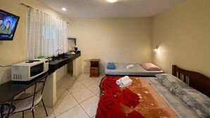 Een hotelkamer met een bed, een bureau met een computer, een magnetron en een televisie.