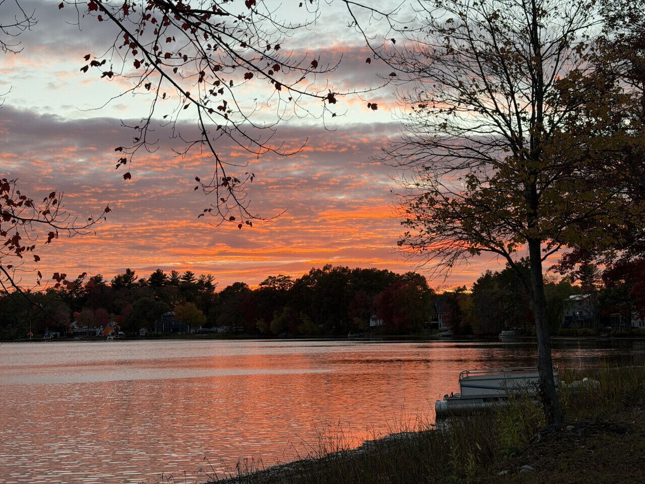 A lake with a sunset, trees, and a dock.