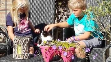 Dos niños sentados en sillas de mimbre al aire libre, con plantas en macetas.