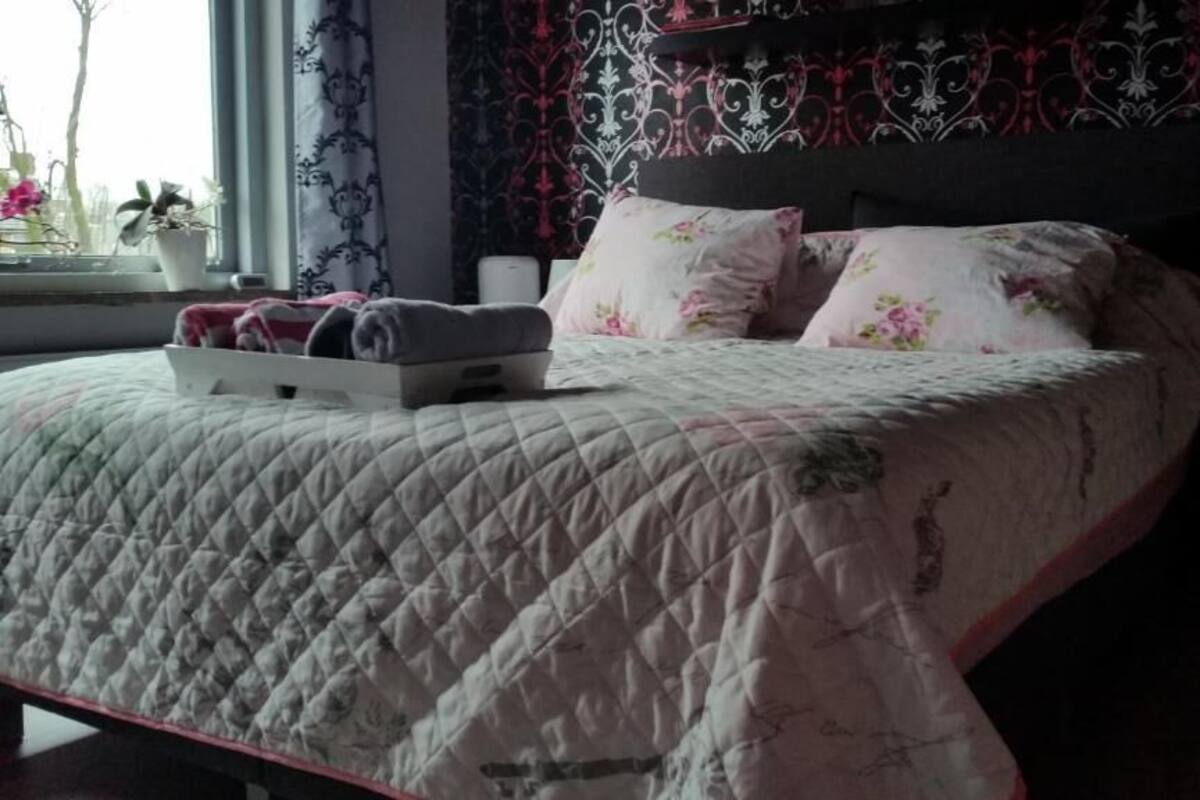 Ein Bett mit gesteppter Bettdecke, zwei Kissen mit Blumenmuster und ein Nachttisch mit einer Lampe.