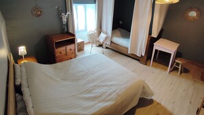 Quarto com cama, mesa de cabeceira, cadeira, mesinha e janela com cortinas.