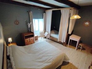 A bedroom with a bed, a bedside table, a chair, a small table, and a window with curtains. - Gîte Estaou Treillo 1 cosy ideal for hikers and lovers of peace and quiet (Le Monastier-sur-Gazeille)