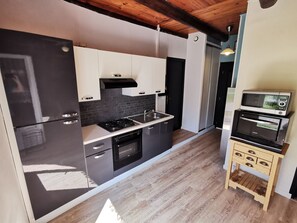 A modern kitchen with black and white cabinetry, a built-in oven, and a microwave on a wooden stand. - Gîte Estaou Treillo 1 cosy ideal for hikers and lovers of peace and quiet (Le Monastier-sur-Gazeille)