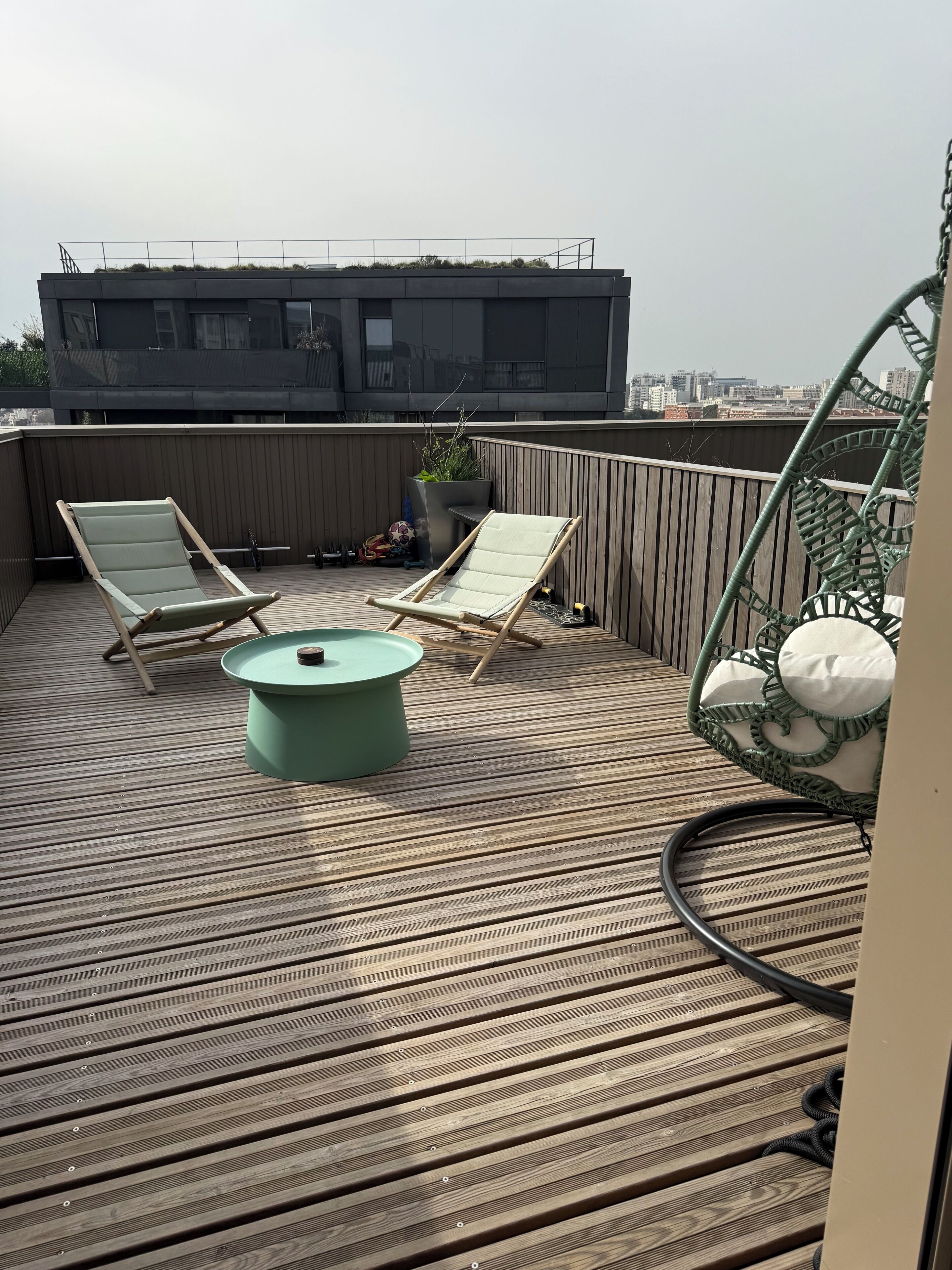 Een terras op het dak met twee loungestoelen, een ronde tafel en een hangstoel.