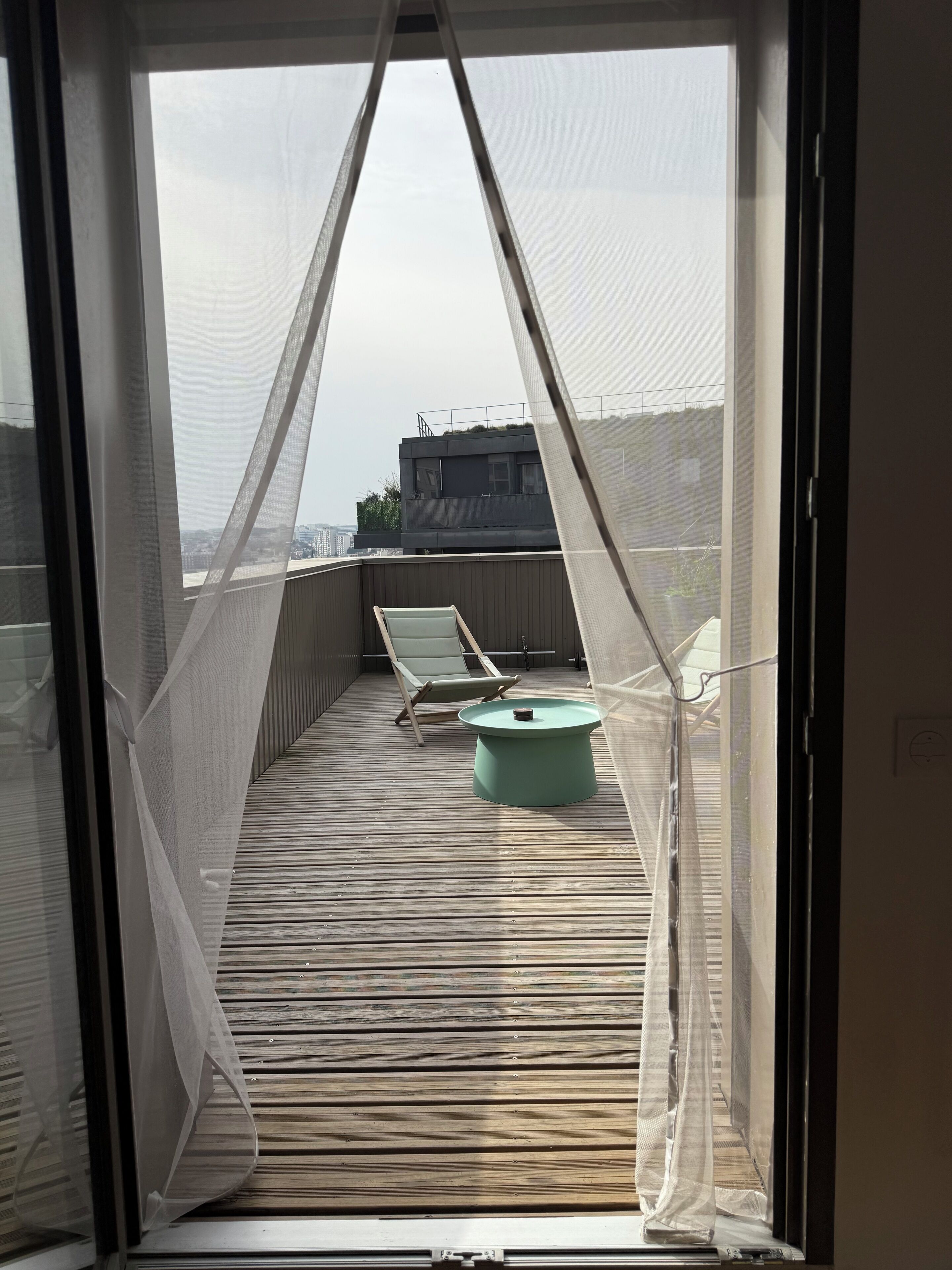 A balcony with a mosquito net, a green table, and a lounge chair.
